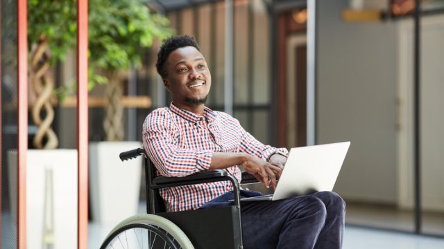 African American, young man, sitting in his wheelchair and working on his laptop as a data entry assistant.