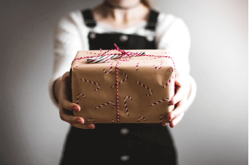 A person holding out a gift wrapped with brown paper with candy canes on it and tied with string, from Virtual Gurus.