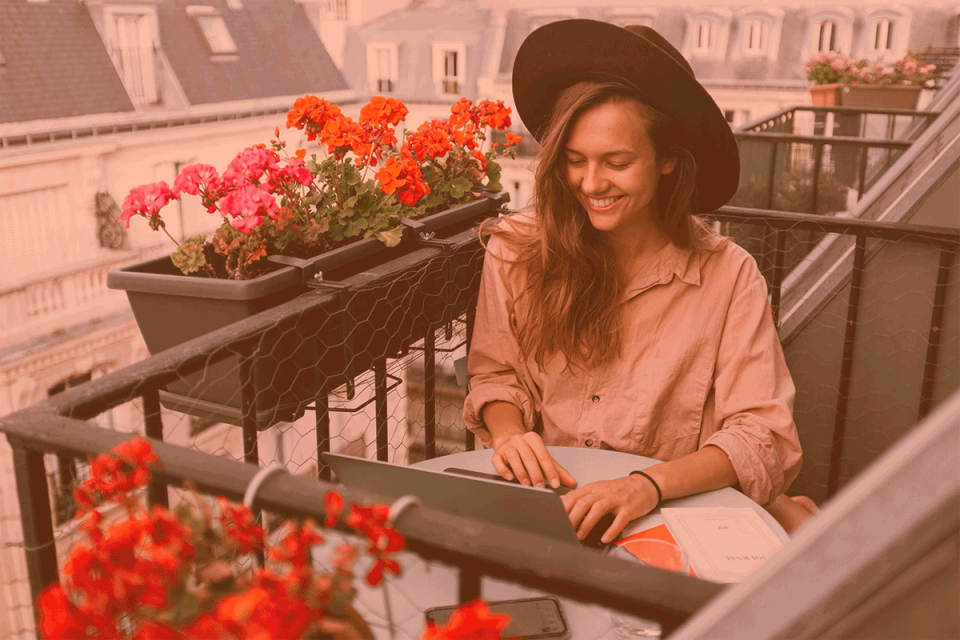 Woman sitting on a balcony in the summer in front of her laptop showing why 2021 is your year to become a virtual assistant with Virtual Gurus.