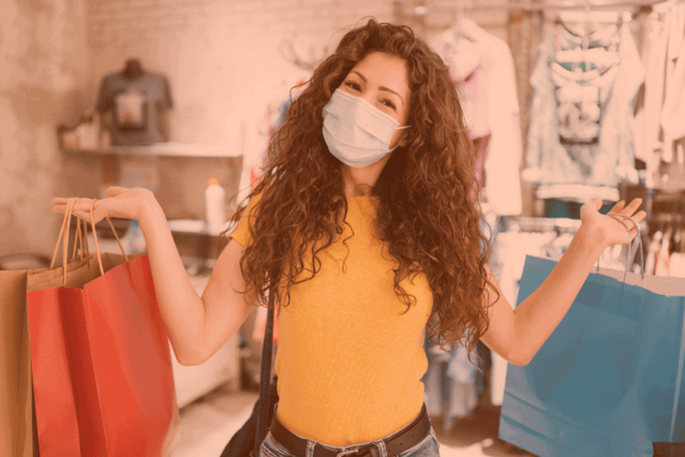 Shopping locally with bags in her hand, a woman wearing a mask and yellow shirt showcases 8 ways you can help small businesses in your community.
