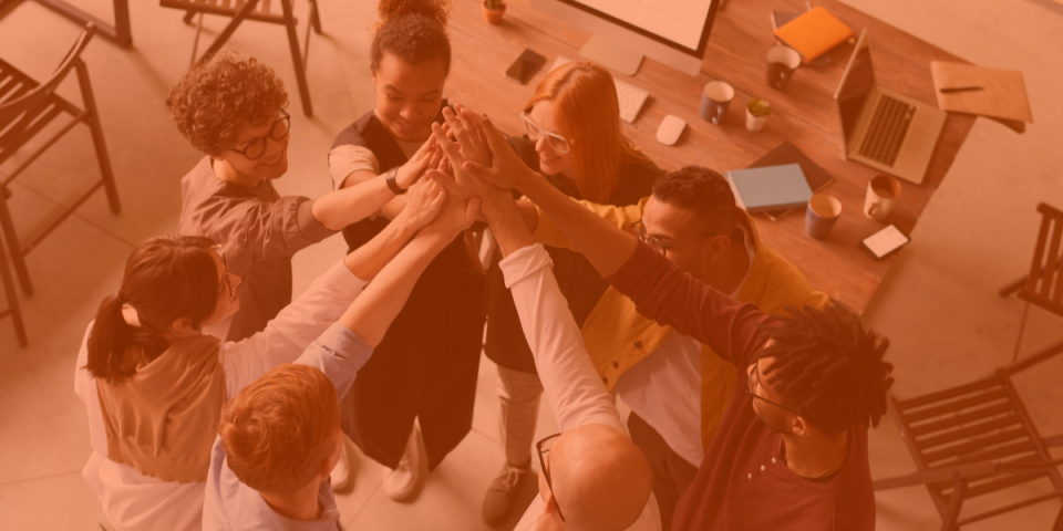 A team of diverse co-workers all giving one big high-five, showing how to add value to a workplace through diversity and inclusion.