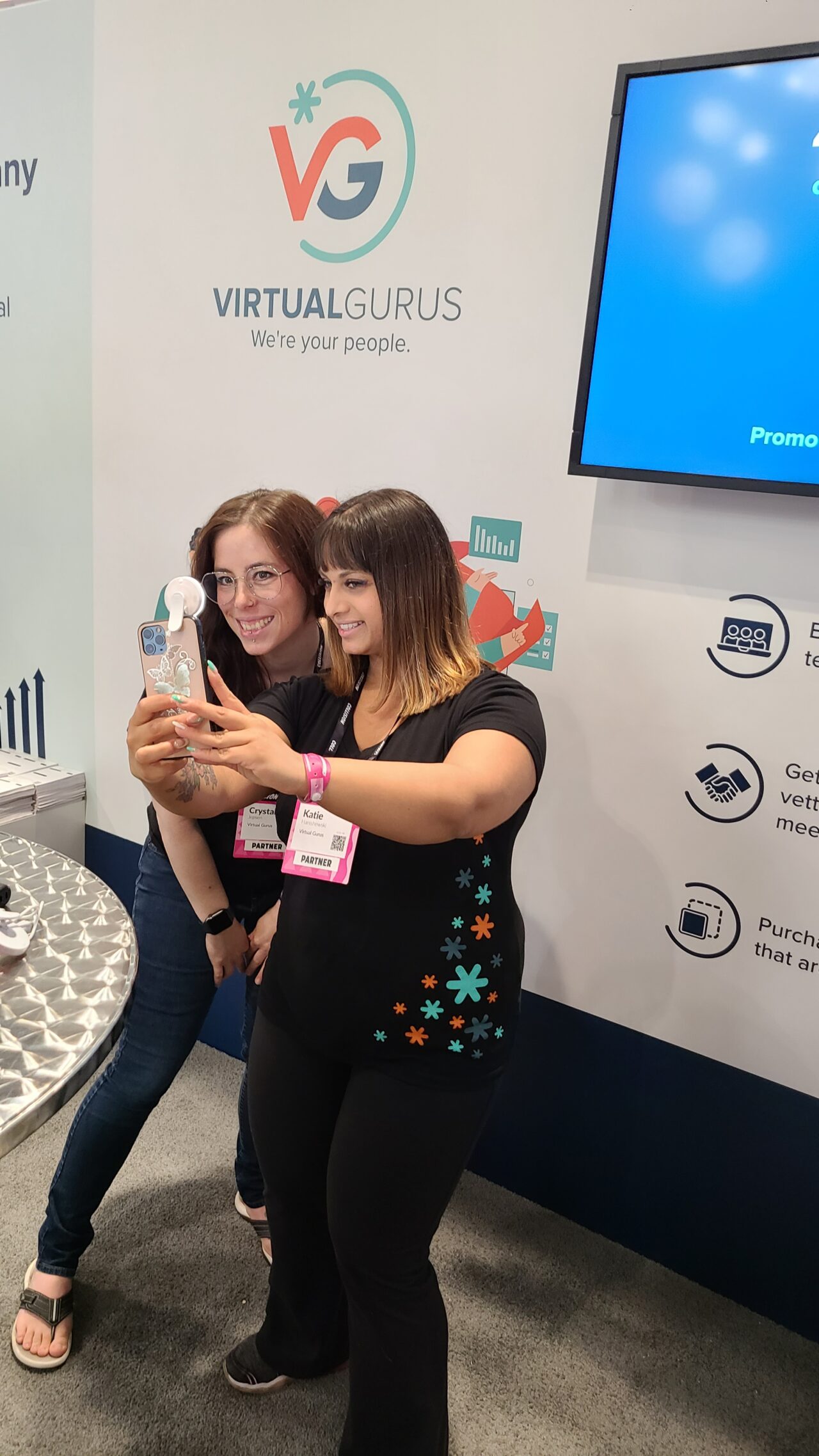 Crystal and Katie, two Virtual Gurus staff members taking a selfie at a trade show booth.