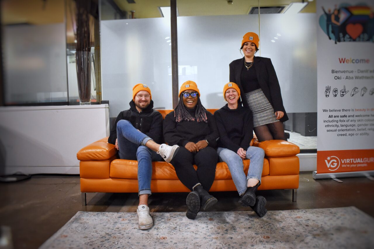 Quatre membres du personnel de Virtual Gurus, divers et heureux, souriant sur un canapé orange au bureau.