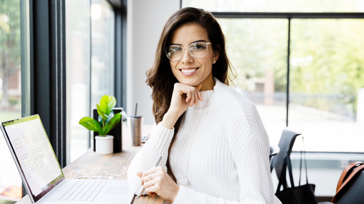 woman with brunette hair, wearing glasses, resting her chin on her hand while sitting in her remote office