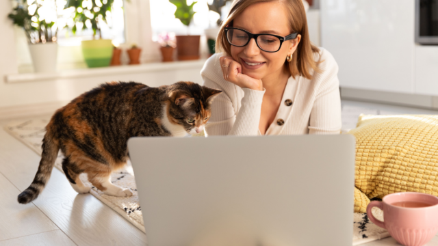 Caucasian woman working on laptop at table with cat cuddling