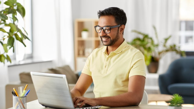 Indian man wearing glasses and smiling as he works as a virtual assistant on his laptop